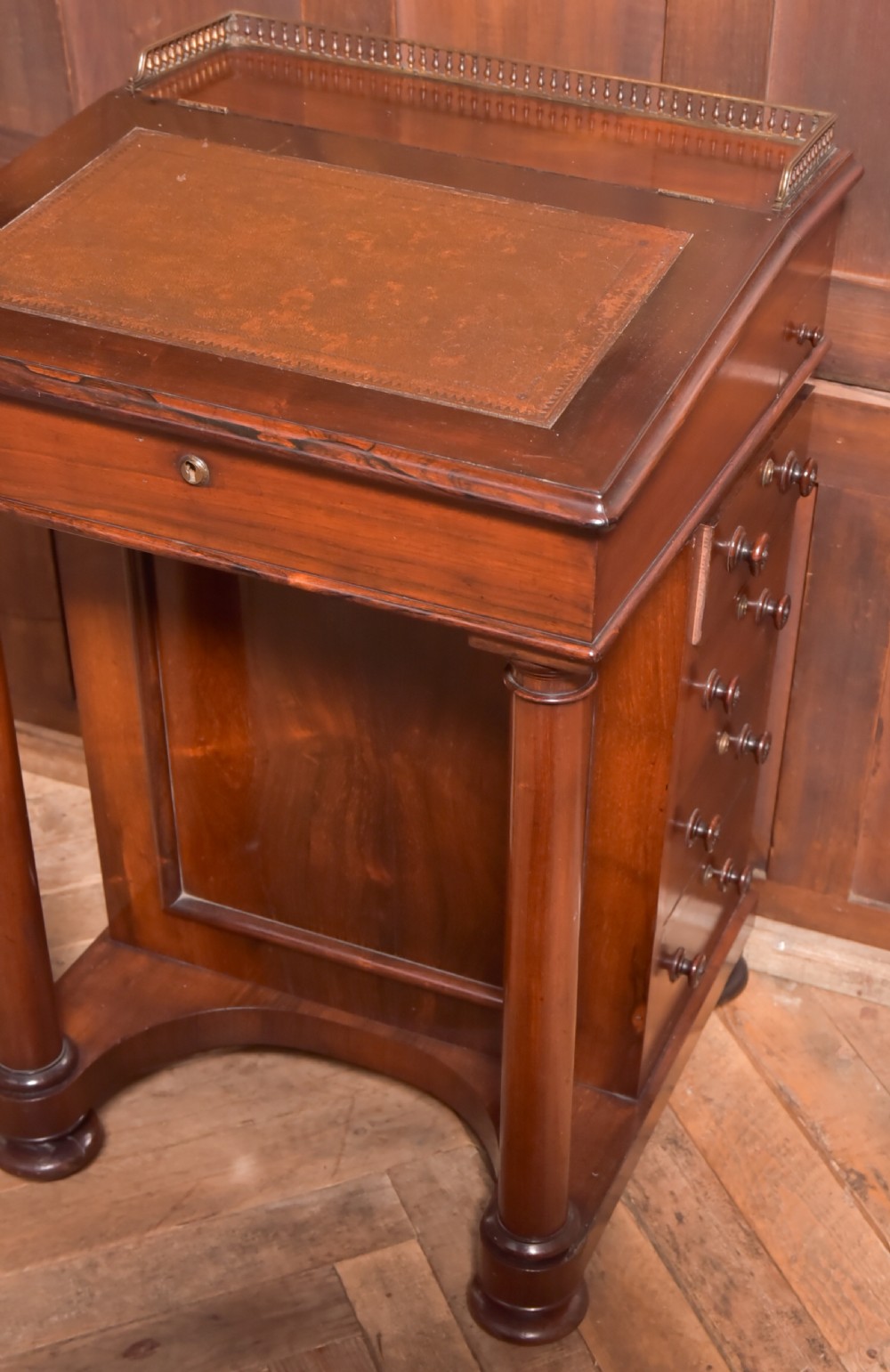 A Victorian rosewood Davenport desk featuring a slanted leather-inset writing surface, brass gallery rail, turned front columns, and side drawers. View X