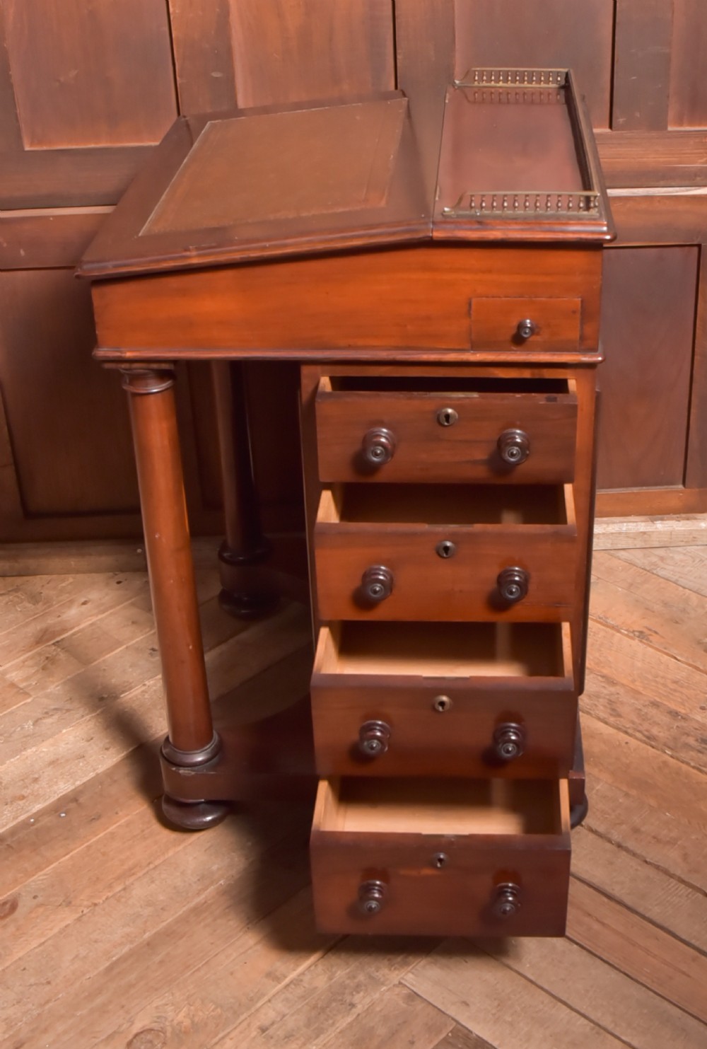 A Victorian rosewood Davenport desk featuring a slanted leather-inset writing surface, brass gallery rail, turned front columns, and side drawers. View XI