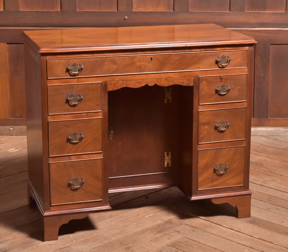 An antique Georgian mahogany kneehole desk featuring seven drawers with brass batwing handles, a recessed central cupboard, and shaped bracket feet.