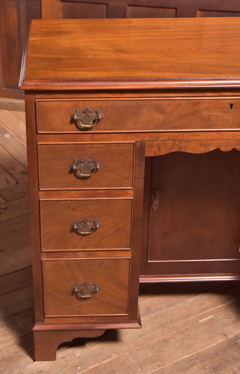 An antique Georgian mahogany kneehole desk featuring seven drawers with brass batwing handles, a recessed central cupboard, and shaped bracket feet. View II