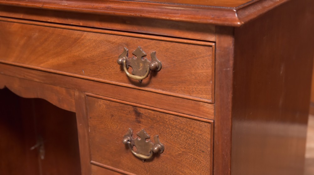 An antique Georgian mahogany kneehole desk featuring seven drawers with brass batwing handles, a recessed central cupboard, and shaped bracket feet. View III