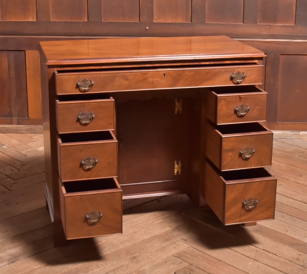 An antique Georgian mahogany kneehole desk featuring seven drawers with brass batwing handles, a recessed central cupboard, and shaped bracket feet. View V