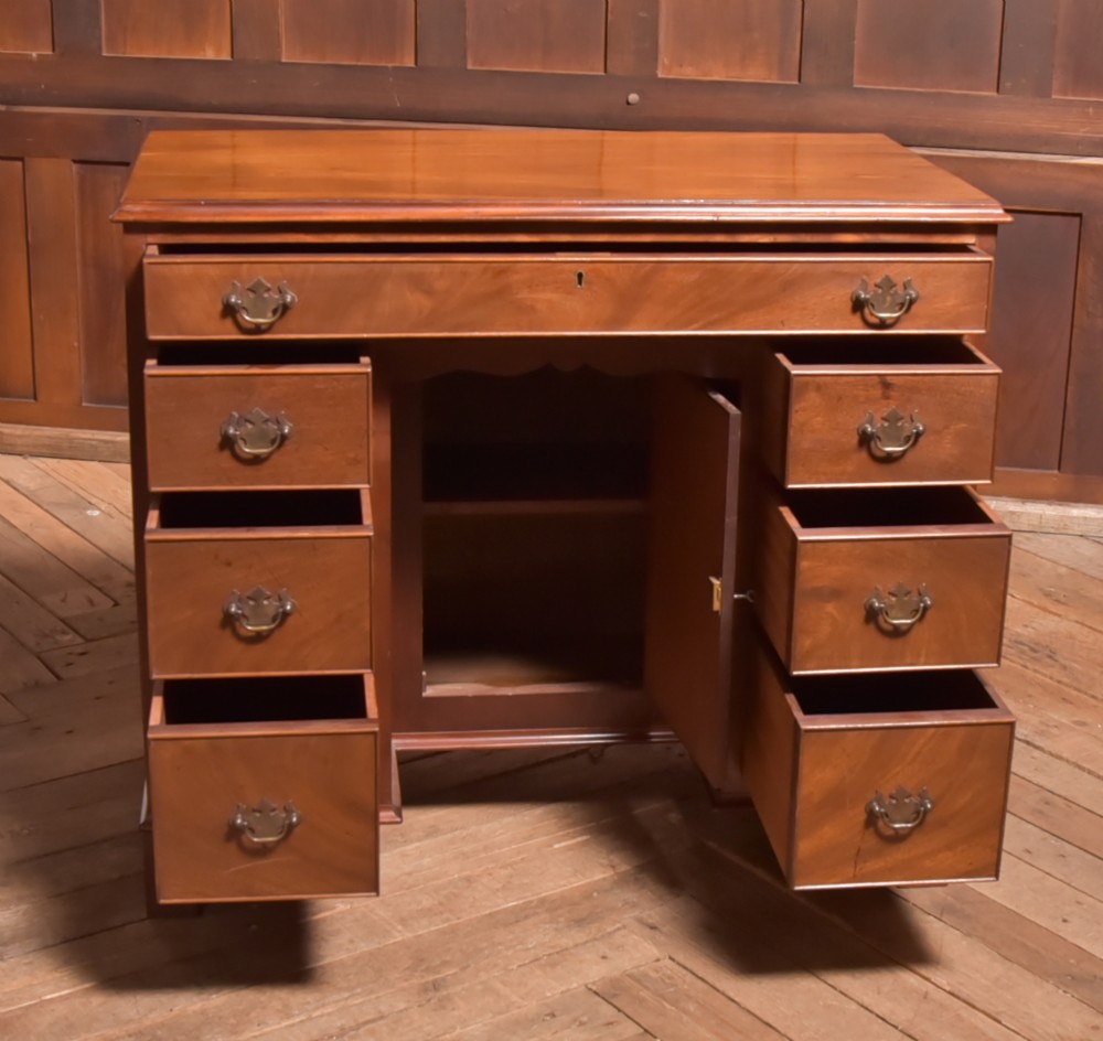 An antique Georgian mahogany kneehole desk featuring seven drawers with brass batwing handles, a recessed central cupboard, and shaped bracket feet. View VI