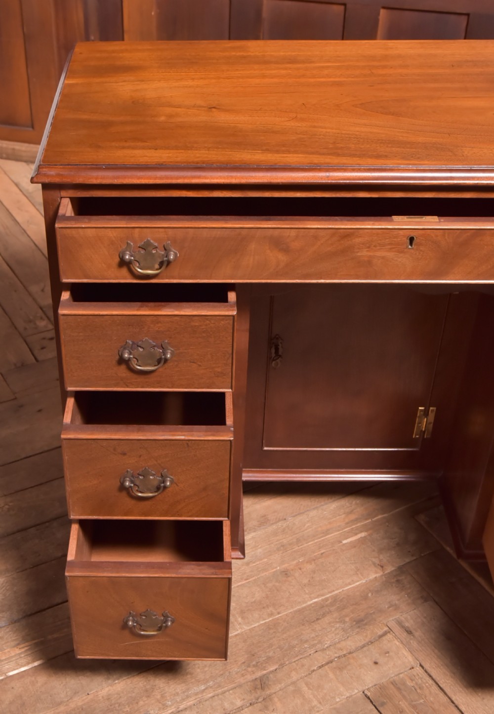 An antique Georgian mahogany kneehole desk featuring seven drawers with brass batwing handles, a recessed central cupboard, and shaped bracket feet. View IX