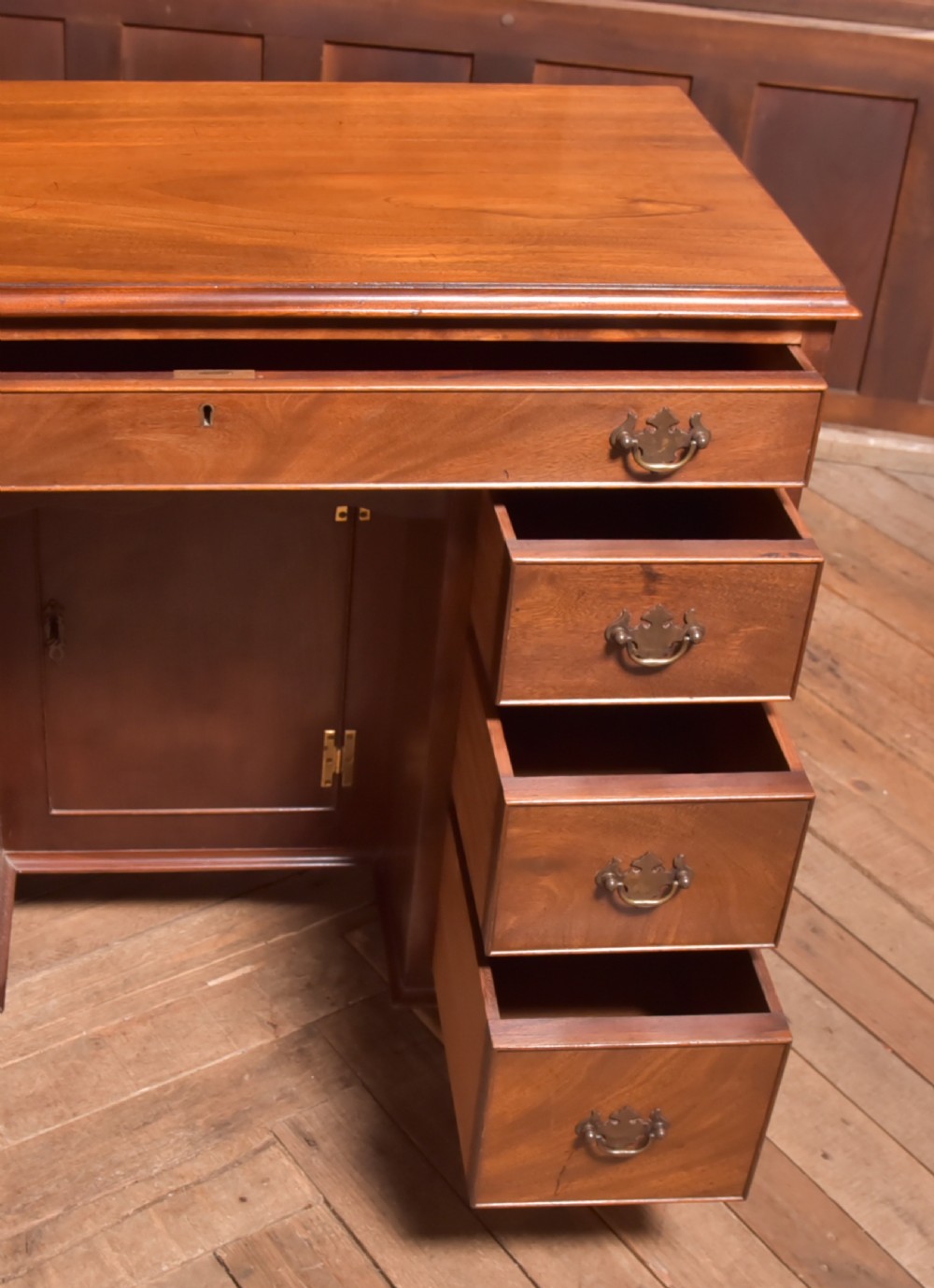 An antique Georgian mahogany kneehole desk featuring seven drawers with brass batwing handles, a recessed central cupboard, and shaped bracket feet. View X