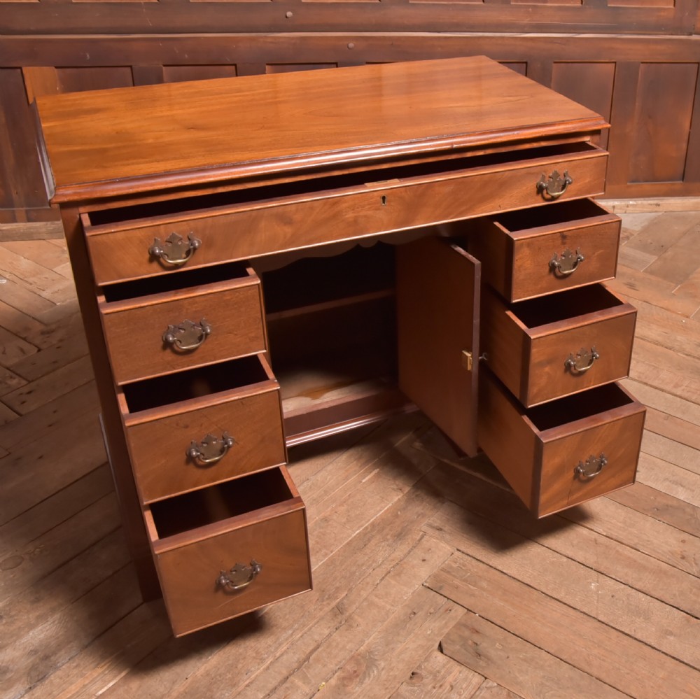 An antique Georgian mahogany kneehole desk featuring seven drawers with brass batwing handles, a recessed central cupboard, and shaped bracket feet. View XI