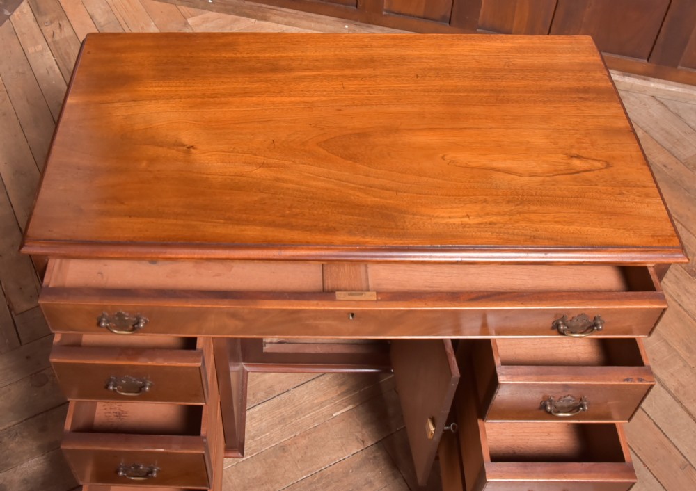 An antique Georgian mahogany kneehole desk featuring seven drawers with brass batwing handles, a recessed central cupboard, and shaped bracket feet. View XII