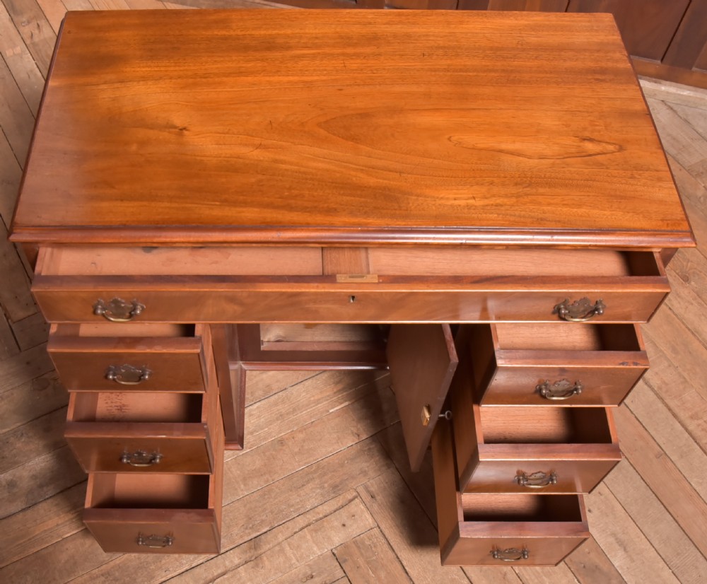An antique Georgian mahogany kneehole desk featuring seven drawers with brass batwing handles, a recessed central cupboard, and shaped bracket feet. View XIII