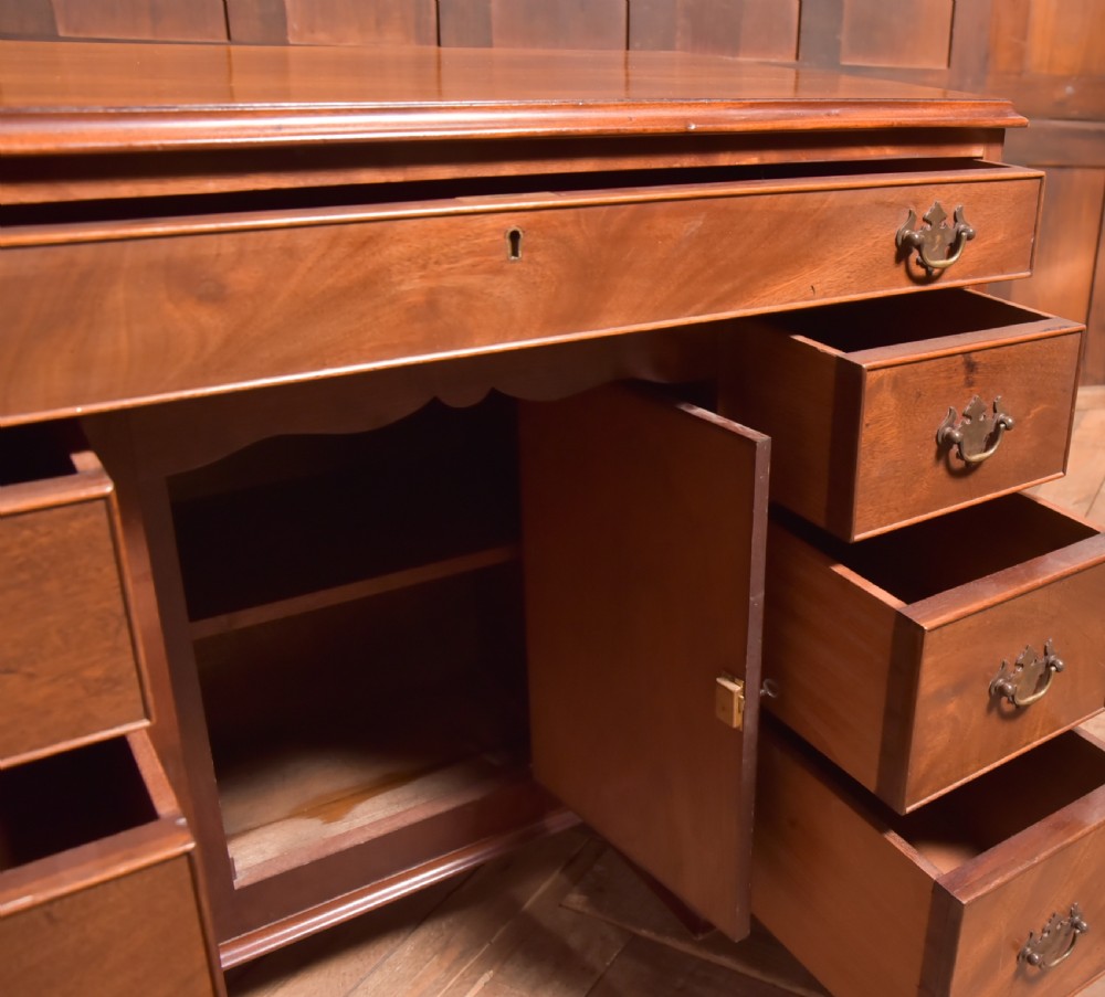 An antique Georgian mahogany kneehole desk featuring seven drawers with brass batwing handles, a recessed central cupboard, and shaped bracket feet. View XIV
