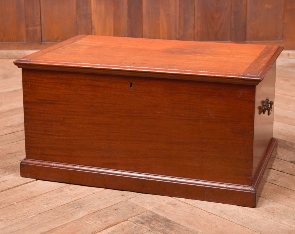 An antique reddish brown mahogany rectangular blanket box featuring a hinged lid, brass side carrying handles, a keyhole, and a moulded plinth base.
