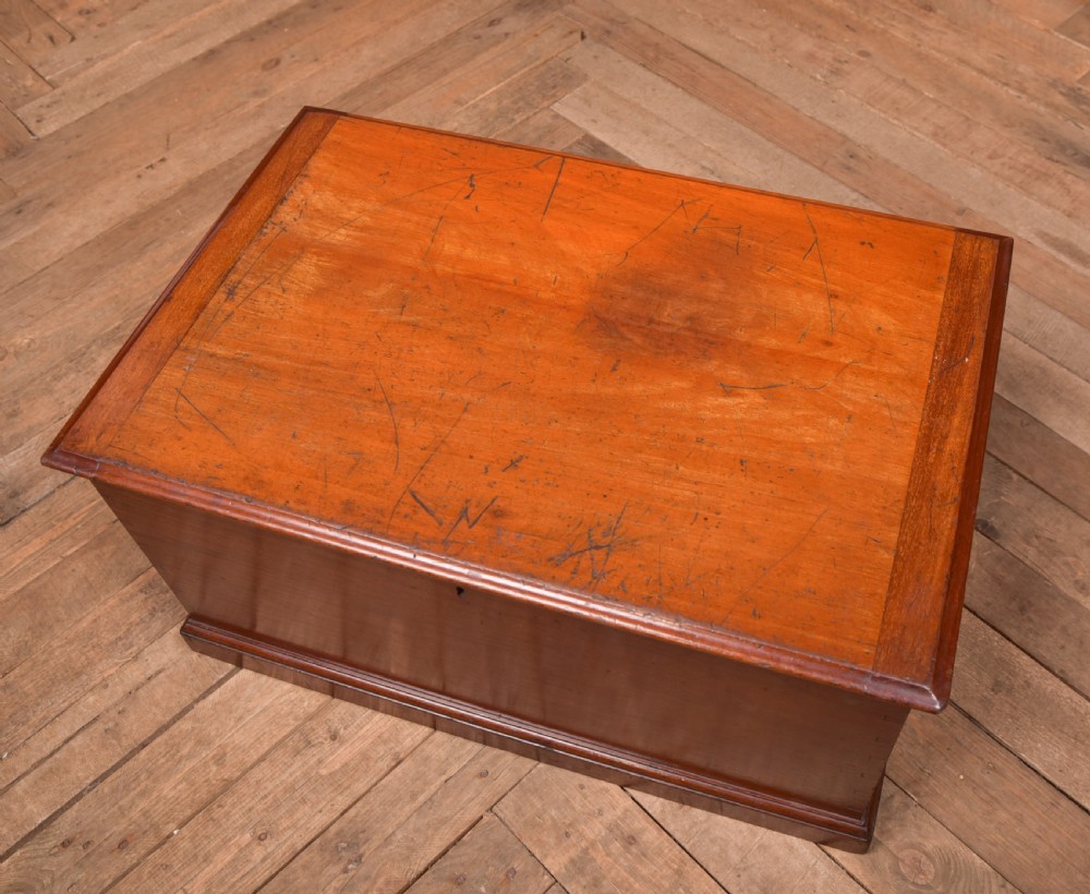 An antique reddish brown mahogany rectangular blanket box featuring a hinged lid, brass side carrying handles, a keyhole, and a moulded plinth base. View II