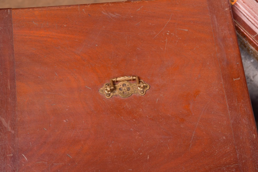 An antique reddish brown mahogany rectangular blanket box featuring a hinged lid, brass side carrying handles, a keyhole, and a moulded plinth base. View III
