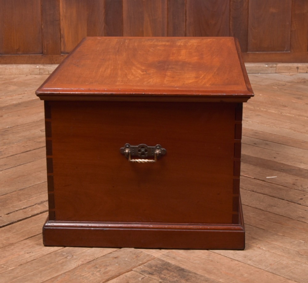 An antique reddish brown mahogany rectangular blanket box featuring a hinged lid, brass side carrying handles, a keyhole, and a moulded plinth base. View XV