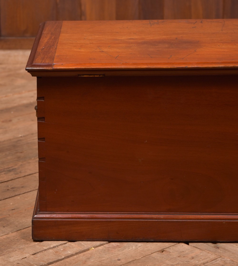 An antique reddish brown mahogany rectangular blanket box featuring a hinged lid, brass side carrying handles, a keyhole, and a moulded plinth base. View XVI