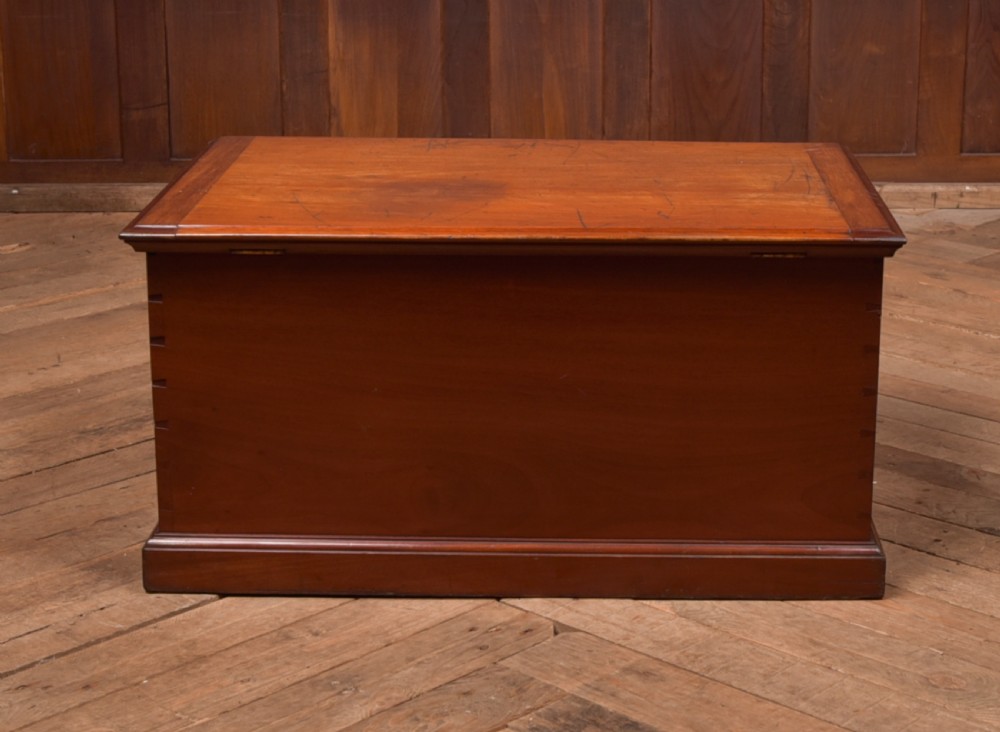 An antique reddish brown mahogany rectangular blanket box featuring a hinged lid, brass side carrying handles, a keyhole, and a moulded plinth base. View XIX