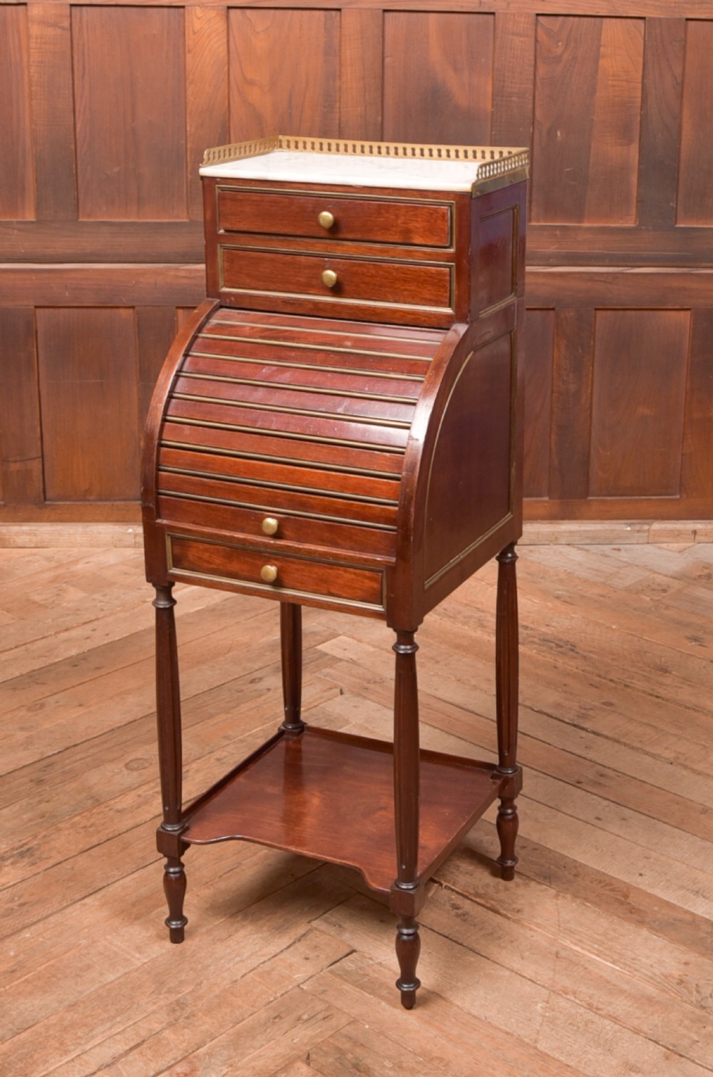 A French mahogany roll-top pot cupboard with a marble top, brass gallery, drawers, slatted tambour front, and turned legs.
