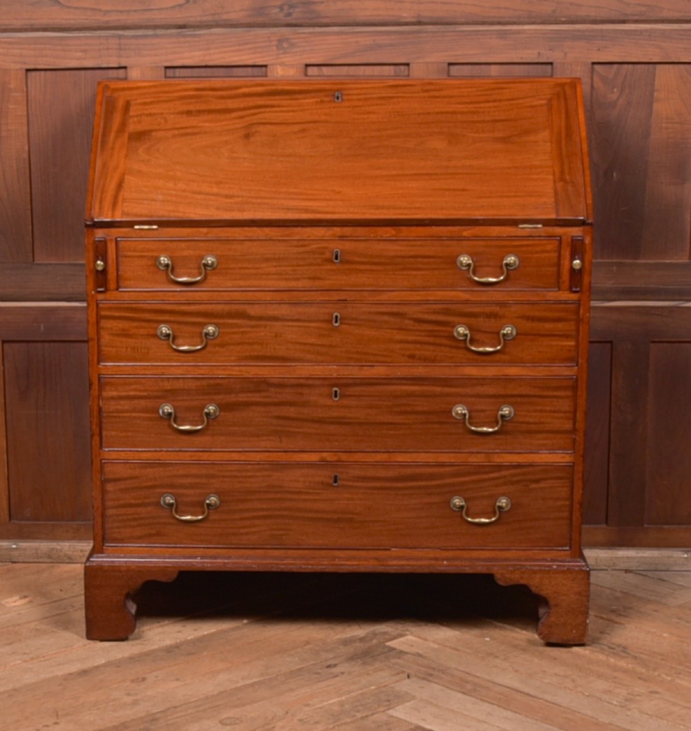 A Georgian mahogany writing bureau featuring a sloped fall-front writing flap above four graduated drawers with brass swan-neck handles and bracket feet.