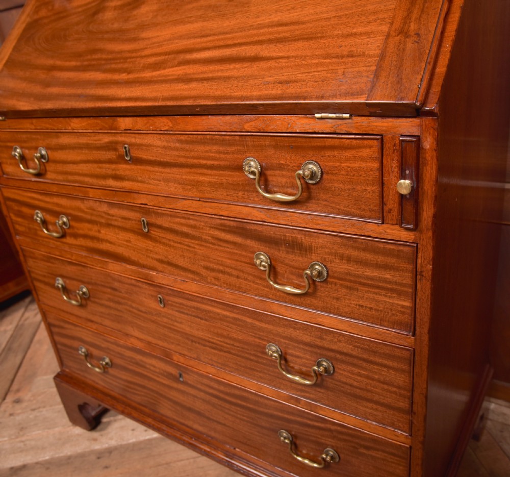 A Georgian mahogany writing bureau featuring a sloped fall-front writing flap above four graduated drawers with brass swan-neck handles and bracket feet. View VI