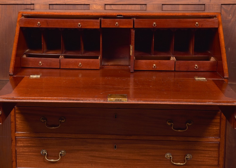 A Georgian mahogany writing bureau featuring a sloped fall-front writing flap above four graduated drawers with brass swan-neck handles and bracket feet. View X