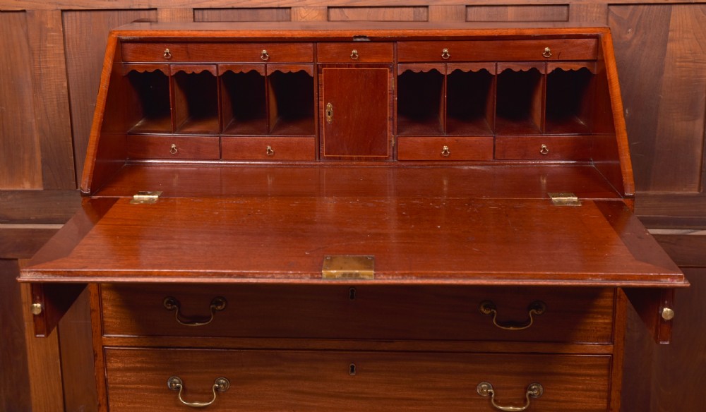 A Georgian mahogany writing bureau featuring a sloped fall-front writing flap above four graduated drawers with brass swan-neck handles and bracket feet. View XV
