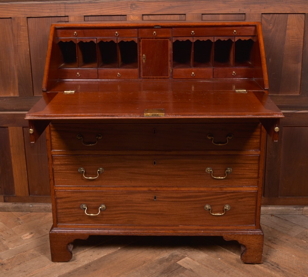 A Georgian mahogany writing bureau featuring a sloped fall-front writing flap above four graduated drawers with brass swan-neck handles and bracket feet. View XVI