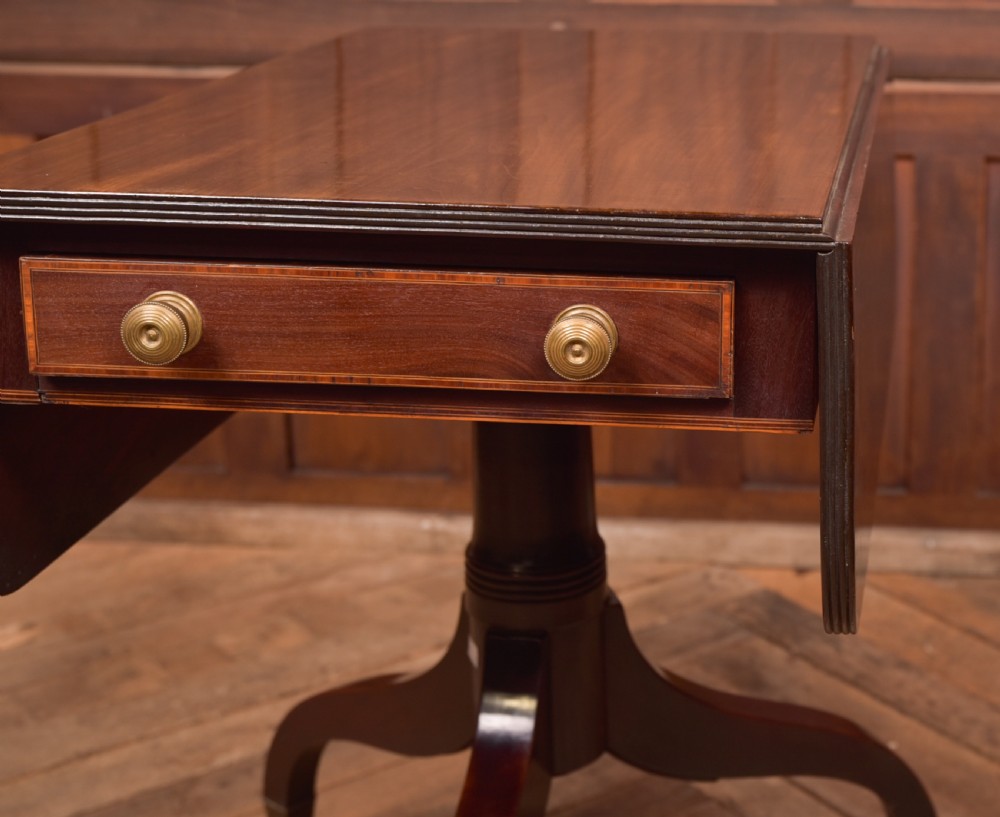 A dark mahogany Regency Pembroke table featuring a drop-leaf top, a single drawer with brass knobs, and a central turned pedestal resting on four splayed legs with brass castors. View V