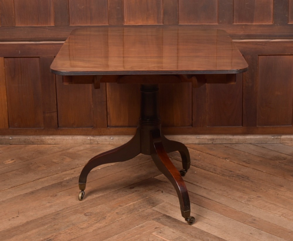 A dark mahogany Regency Pembroke table featuring a drop-leaf top, a single drawer with brass knobs, and a central turned pedestal resting on four splayed legs with brass castors. View VIII
