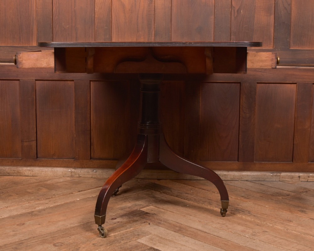 A dark mahogany Regency Pembroke table featuring a drop-leaf top, a single drawer with brass knobs, and a central turned pedestal resting on four splayed legs with brass castors. View XI