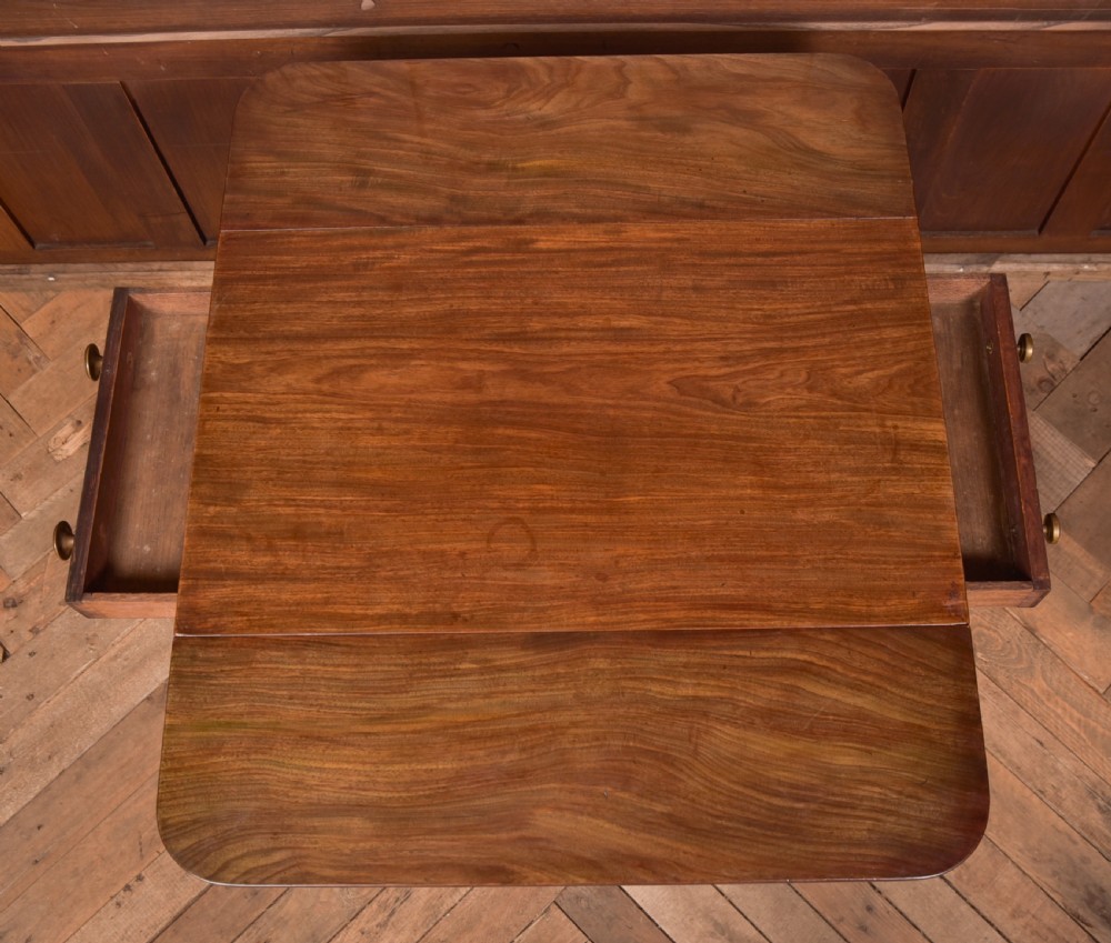A dark mahogany Regency Pembroke table featuring a drop-leaf top, a single drawer with brass knobs, and a central turned pedestal resting on four splayed legs with brass castors. View XII