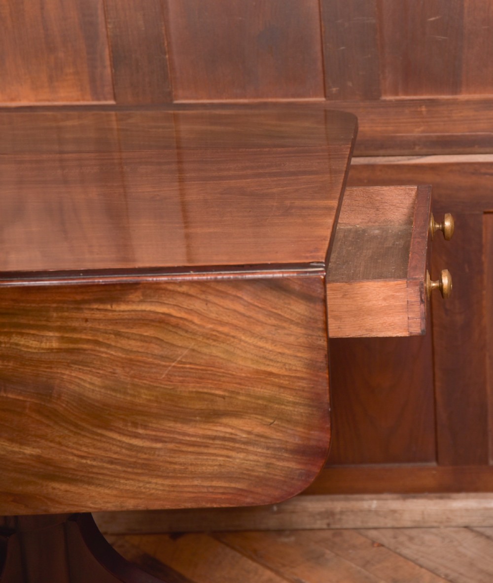 A dark mahogany Regency Pembroke table featuring a drop-leaf top, a single drawer with brass knobs, and a central turned pedestal resting on four splayed legs with brass castors. View XIII