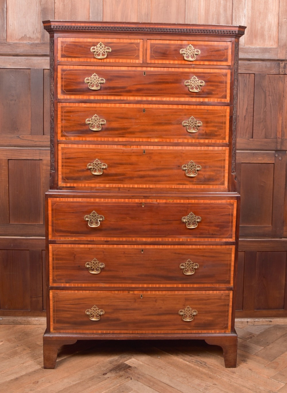 A tall Georgian mahogany chest on chest featuring inlaid drawer borders, brass handles, dentil cornice detail, and bracket feet.