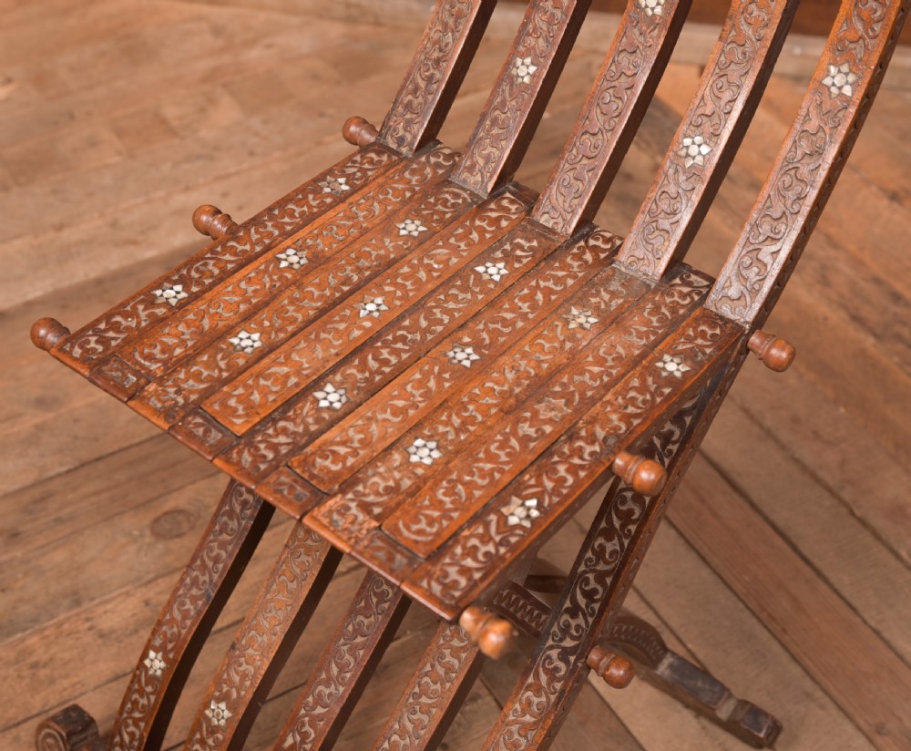 An intricate carved brown wooden Islamic folding chair decorated with mother-of-pearl inlay and calligraphic details. View III