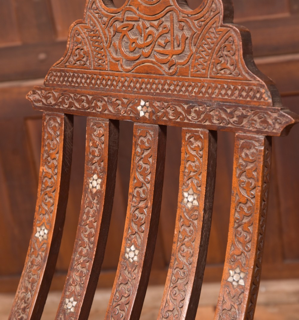 An intricate carved brown wooden Islamic folding chair decorated with mother-of-pearl inlay and calligraphic details. View V