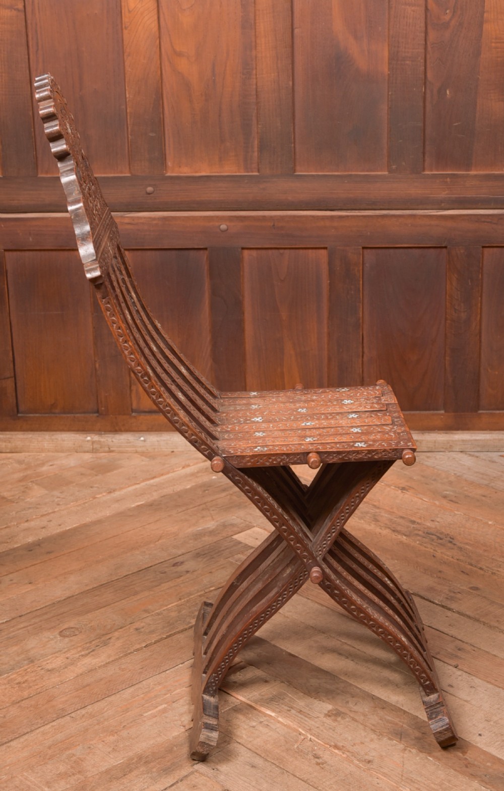 An intricate carved brown wooden Islamic folding chair decorated with mother-of-pearl inlay and calligraphic details. View VI