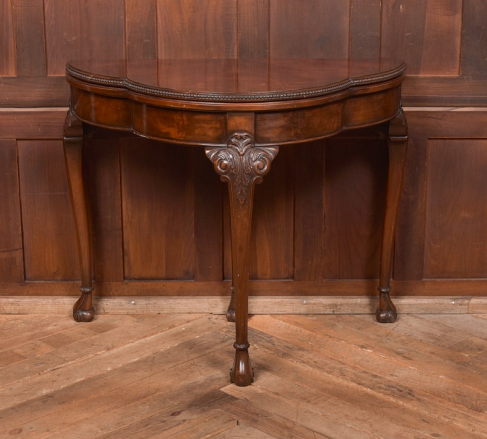 An Edwardian mahogany demi-lune card table featuring carved cabriole legs and a polished fold-over top.