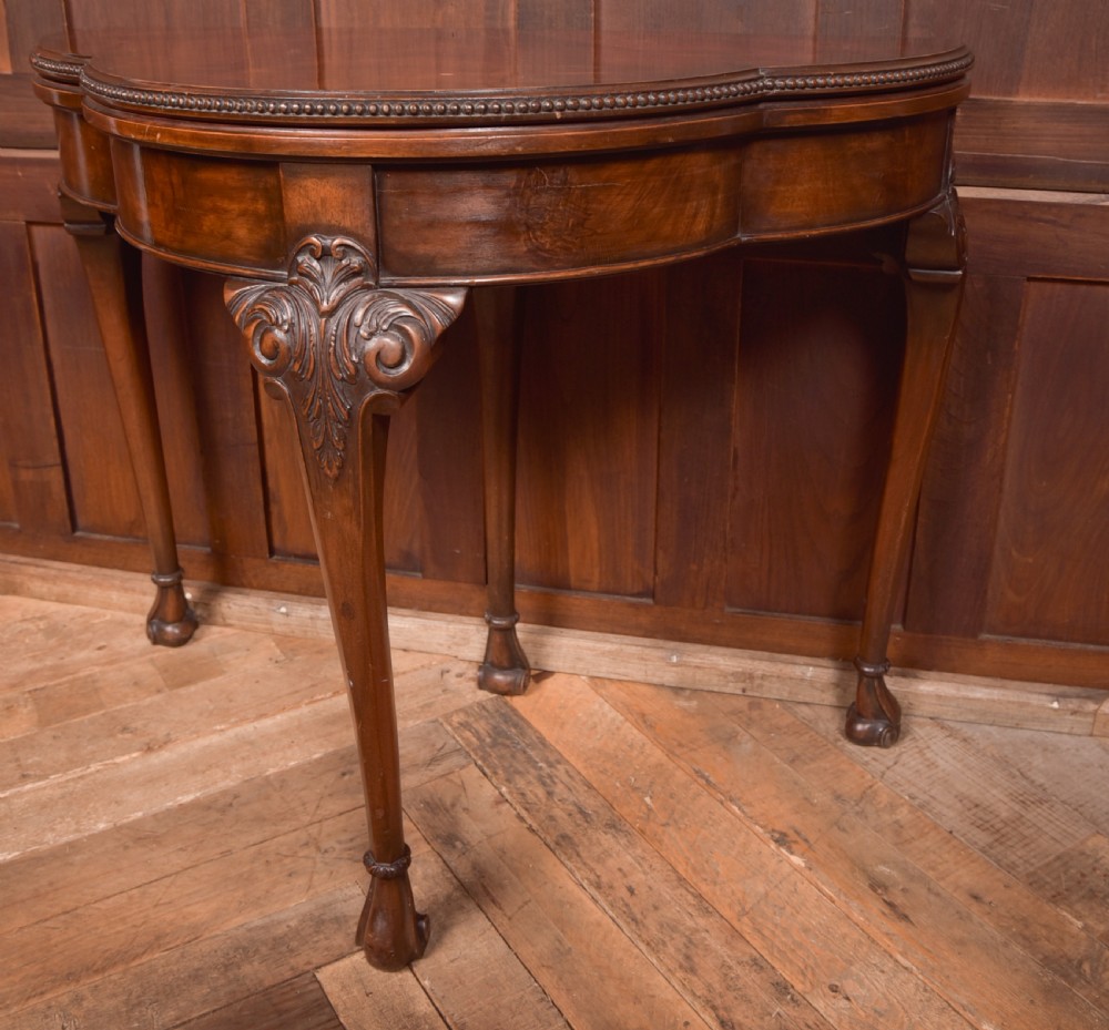 An Edwardian mahogany demi-lune card table featuring carved cabriole legs and a polished fold-over top. View V