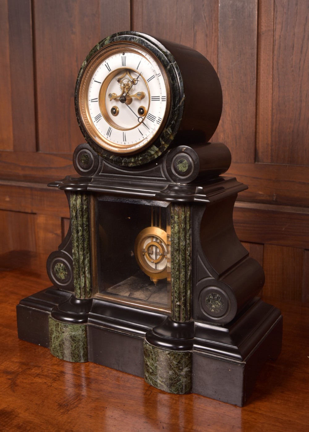 A Victorian French black slate and green marble mantel clock featuring a white enamel dial with Roman numerals and a visible brass pendulum behind glass. View III