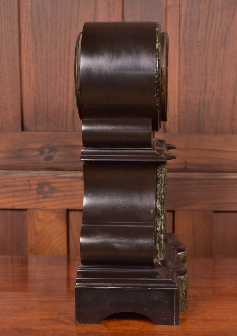 A Victorian French black slate and green marble mantel clock featuring a white enamel dial with Roman numerals and a visible brass pendulum behind glass. View VIII