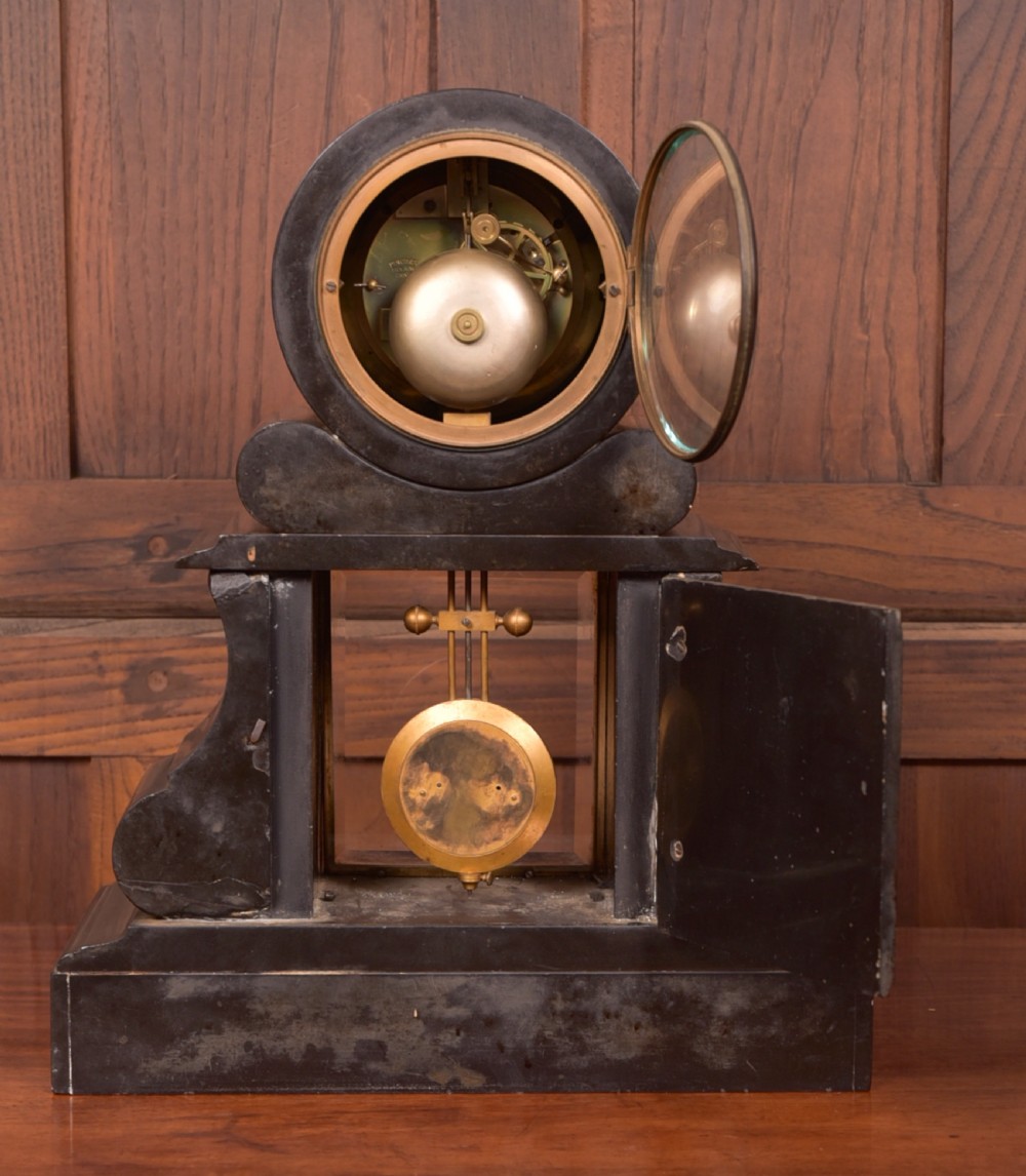 A Victorian French black slate and green marble mantel clock featuring a white enamel dial with Roman numerals and a visible brass pendulum behind glass. View IX