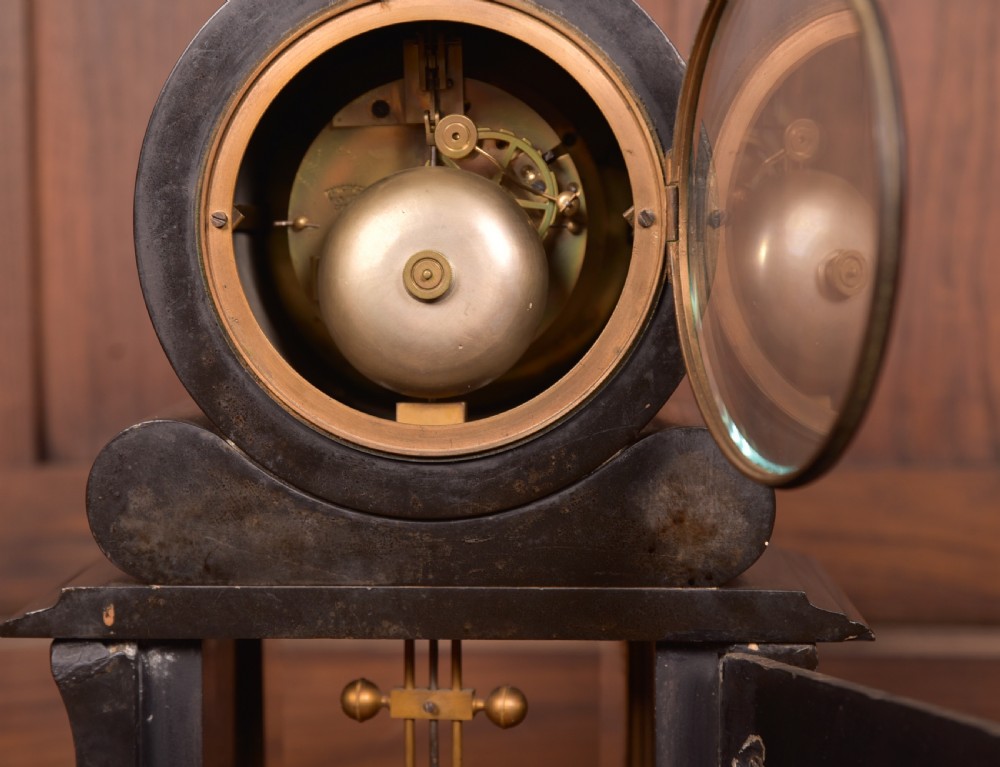 A Victorian French black slate and green marble mantel clock featuring a white enamel dial with Roman numerals and a visible brass pendulum behind glass. View X