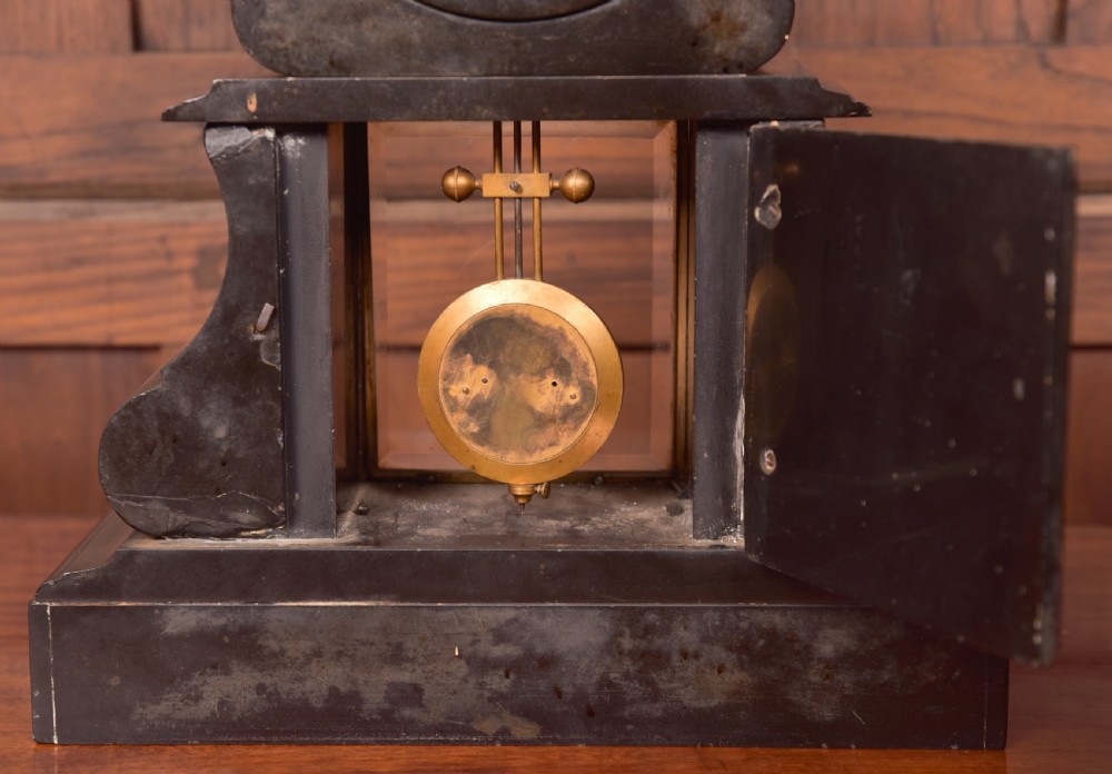A Victorian French black slate and green marble mantel clock featuring a white enamel dial with Roman numerals and a visible brass pendulum behind glass. View XI