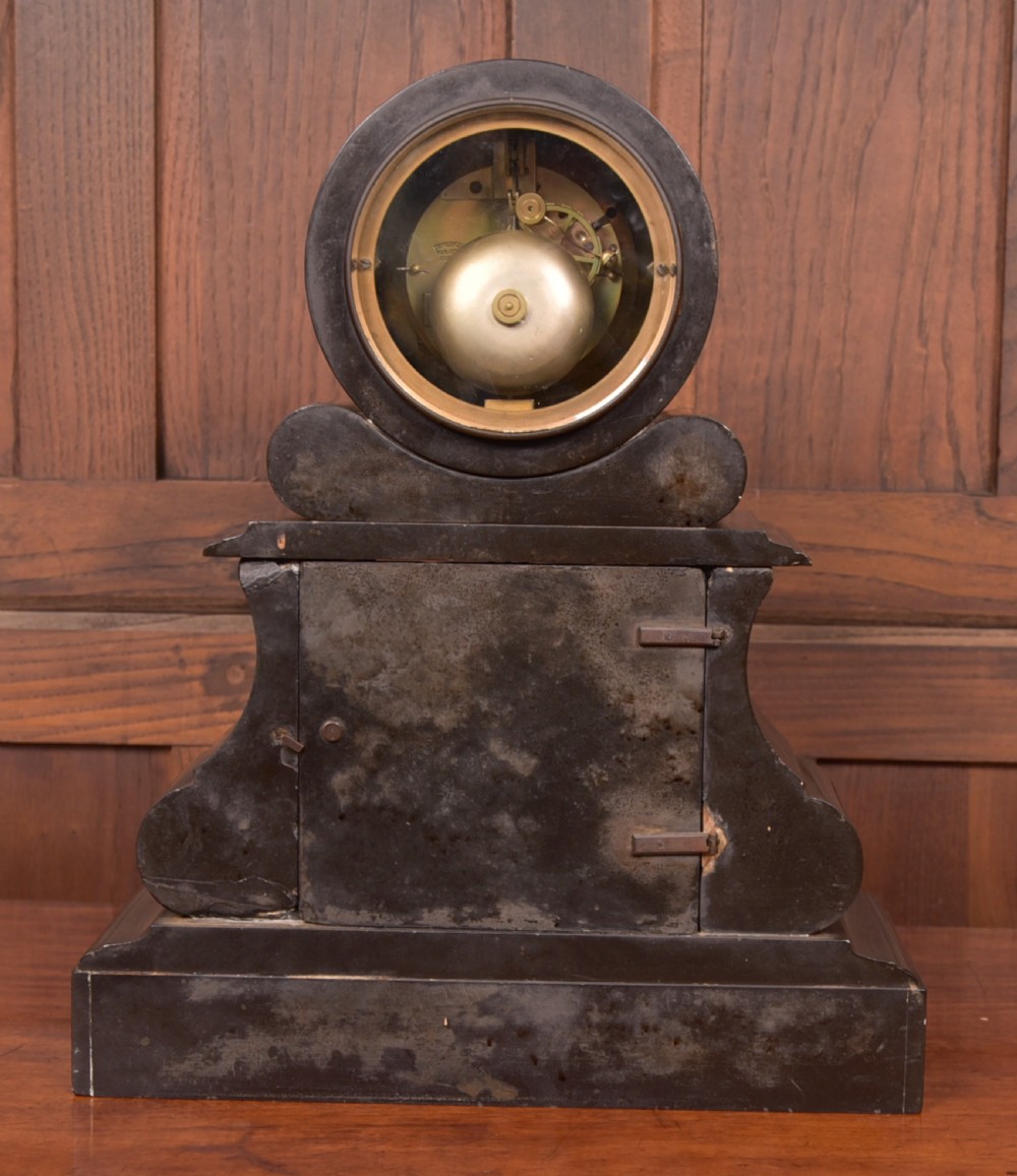 A Victorian French black slate and green marble mantel clock featuring a white enamel dial with Roman numerals and a visible brass pendulum behind glass. View XII