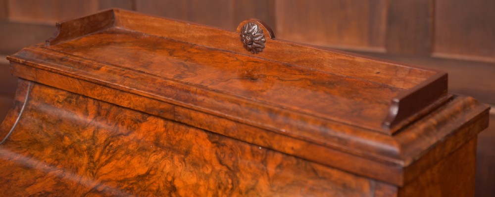 A Victorian burr walnut piano top davenport desk featuring a rounded sloping lid, carved scroll supports, and side drawers with turned wooden knobs. View II