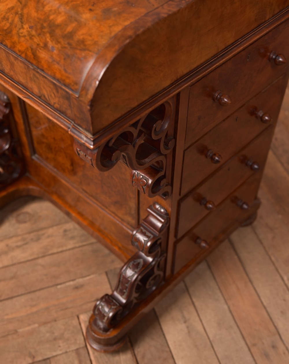 A Victorian burr walnut piano top davenport desk featuring a rounded sloping lid, carved scroll supports, and side drawers with turned wooden knobs. View III