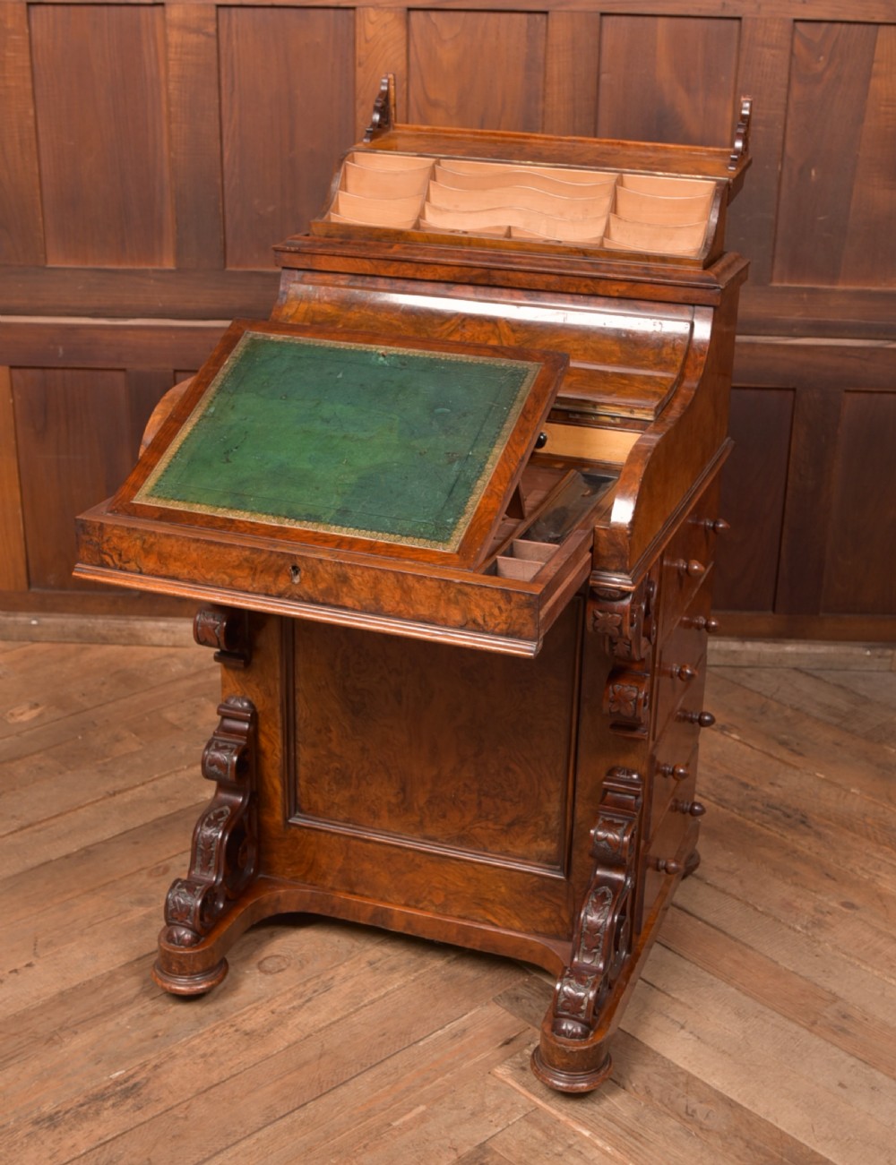 A Victorian burr walnut piano top davenport desk featuring a rounded sloping lid, carved scroll supports, and side drawers with turned wooden knobs. View VI