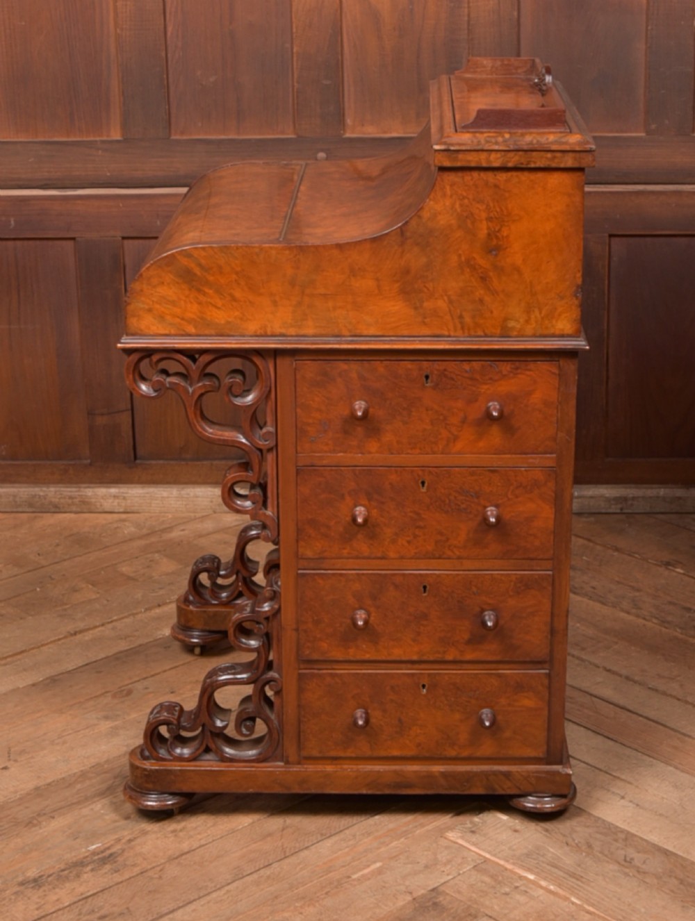 A Victorian burr walnut piano top davenport desk featuring a rounded sloping lid, carved scroll supports, and side drawers with turned wooden knobs. View IX