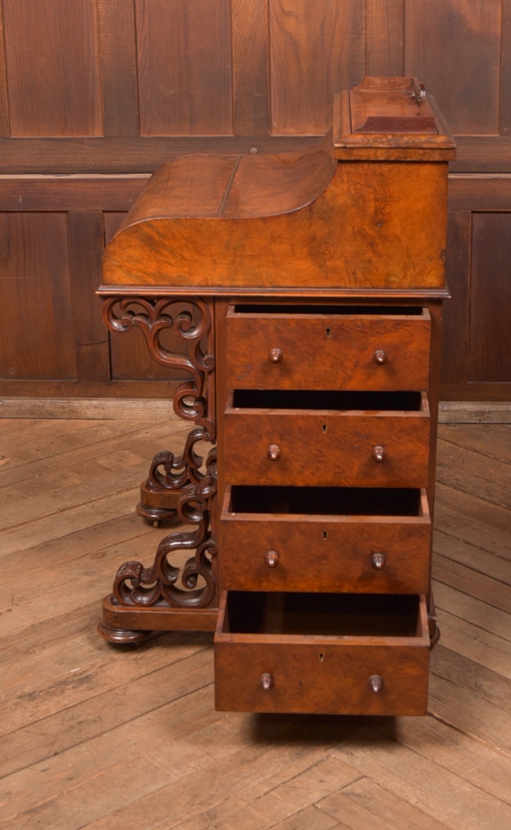 A Victorian burr walnut piano top davenport desk featuring a rounded sloping lid, carved scroll supports, and side drawers with turned wooden knobs. View X