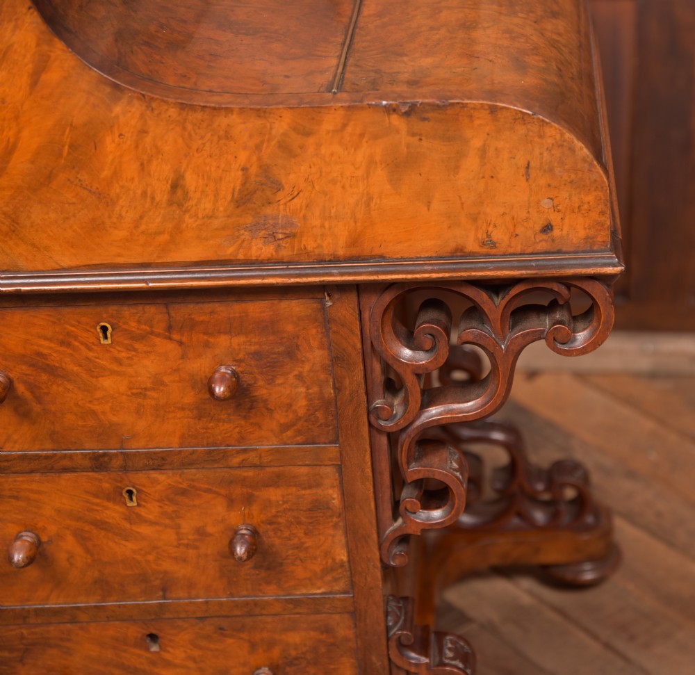 A Victorian burr walnut piano top davenport desk featuring a rounded sloping lid, carved scroll supports, and side drawers with turned wooden knobs. View XIV
