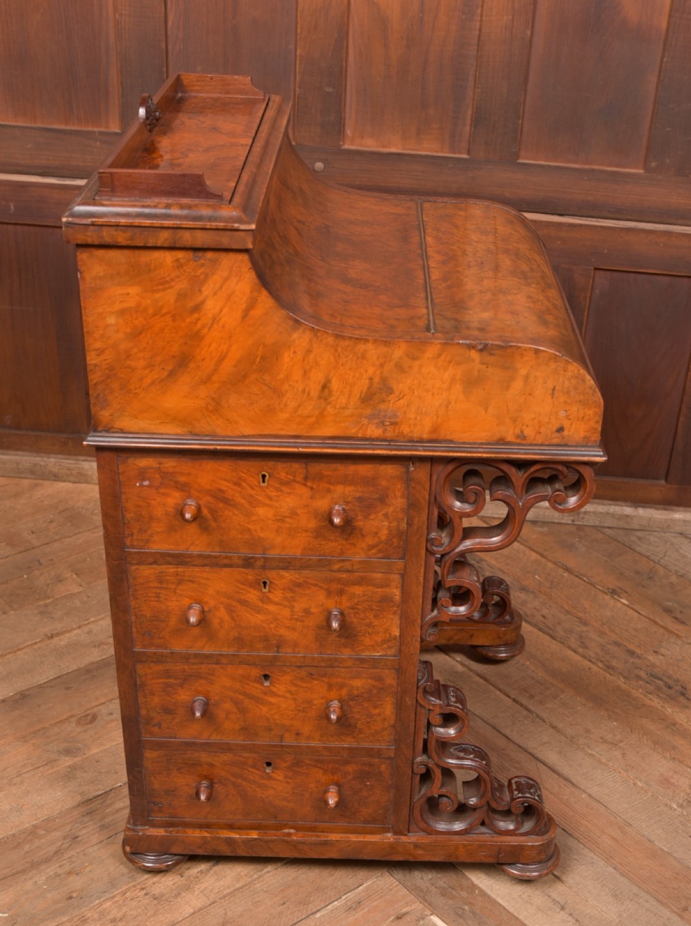 A Victorian burr walnut piano top davenport desk featuring a rounded sloping lid, carved scroll supports, and side drawers with turned wooden knobs. View XV