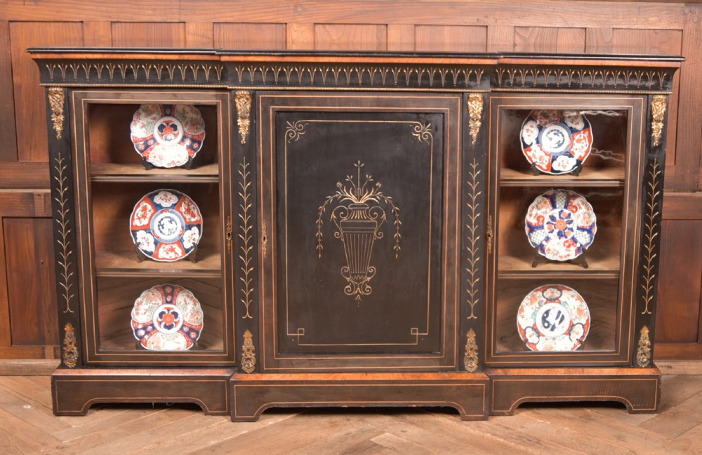 A Victorian ebonised breakfront credenza featuring glazed side doors, gilt incised urn motifs, and cast decorative mounts.